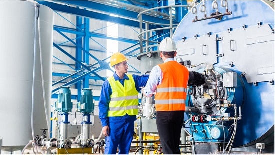 Two geothermal power plan technicians looking at heat gauges in a warehouse.